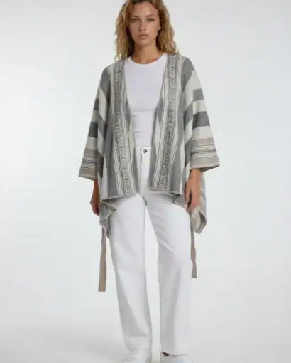 Donna indossa un maglione invernale con motivo etnico, cardigan aperto e pantaloni bianchi, in uno stile casual e elegante.