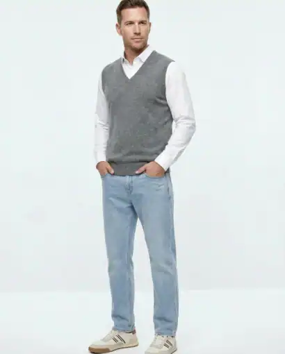 Uomo elegante indossa un maglione grigio a V e jeans chiari, in un ambiente minimalista, promuovendo abbigliamento di qualità.