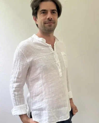 Uomo con capelli castani e barba, indossa una camicia di lino bianco, stile casual elegante, perfetta per look estivi e casual.