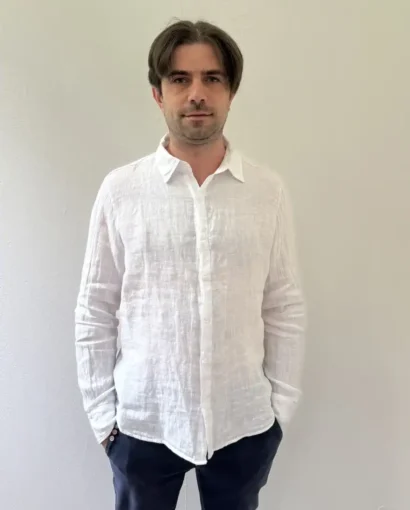 Uomo con camicia di lino bianco, stile elegante e casual, in un ambiente neutro. Perfetta per look estivi e casual, rappresenta la qualità e l'artigianato del Maglificio Annamaria.
