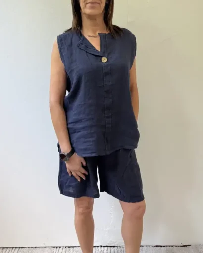 Donna in abbigliamento casual, vestita con top senza maniche e pantaloncini in tessuto denim, posa in un ambiente neutro.