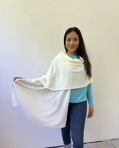 Donna con scialle in lana bianca, abbigliamento elegante e caldo, indossato con maglietta azzurra e jeans, in un ambiente neutro.