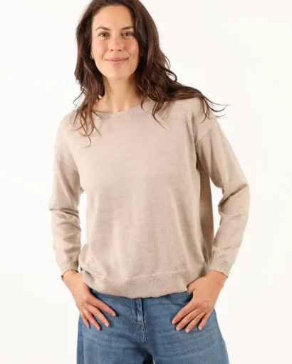 Donna sorridente indossa un maglione beige e jeans blu, rappresentando l'eleganza casual di Maglificio Annamaria, specializzato in maglieria di alta qualità in Italia.