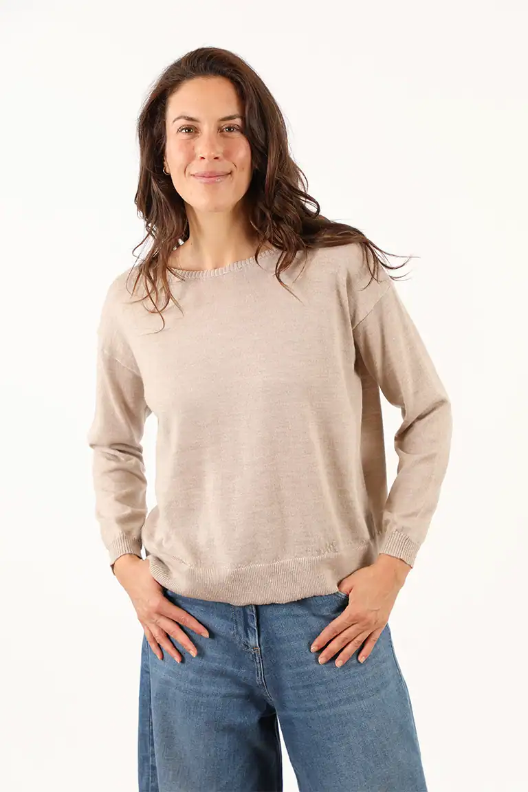 Donna sorridente indossa un maglione beige e jeans blu, rappresentando l'eleganza casual di Maglificio Annamaria, specializzato in maglieria di alta qualità in Italia.