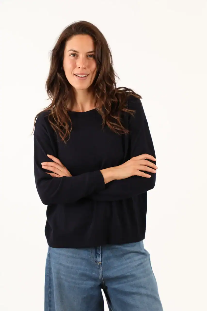 Donna sorridente indossa un maglione nero e jeans, rappresentando l'eleganza casuale di Maglificio Annamaria, specializzato in maglieria di alta qualità in Italia.