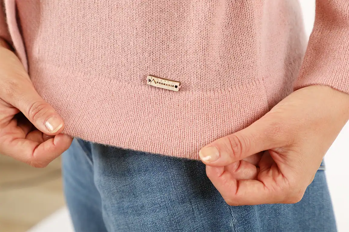 Dettaglio di un maglione rosa con etichetta Maglificio Annamaria, tessuto morbido e di alta qualità, perfetto per un look elegante e confortevole.
