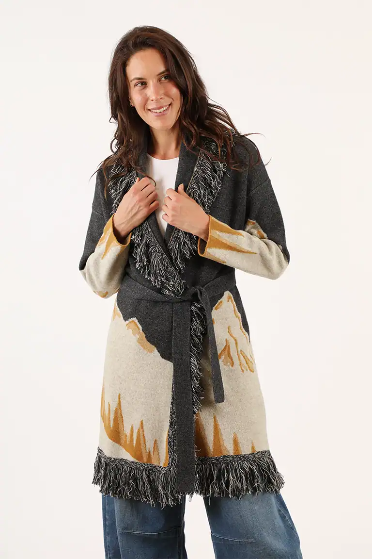 Donna indossa un cappotto in lana con motivo astratto in beige, grigio e nero, con frange sul bordo, perfetto per l'inverno, da Maglificio Annamaria.