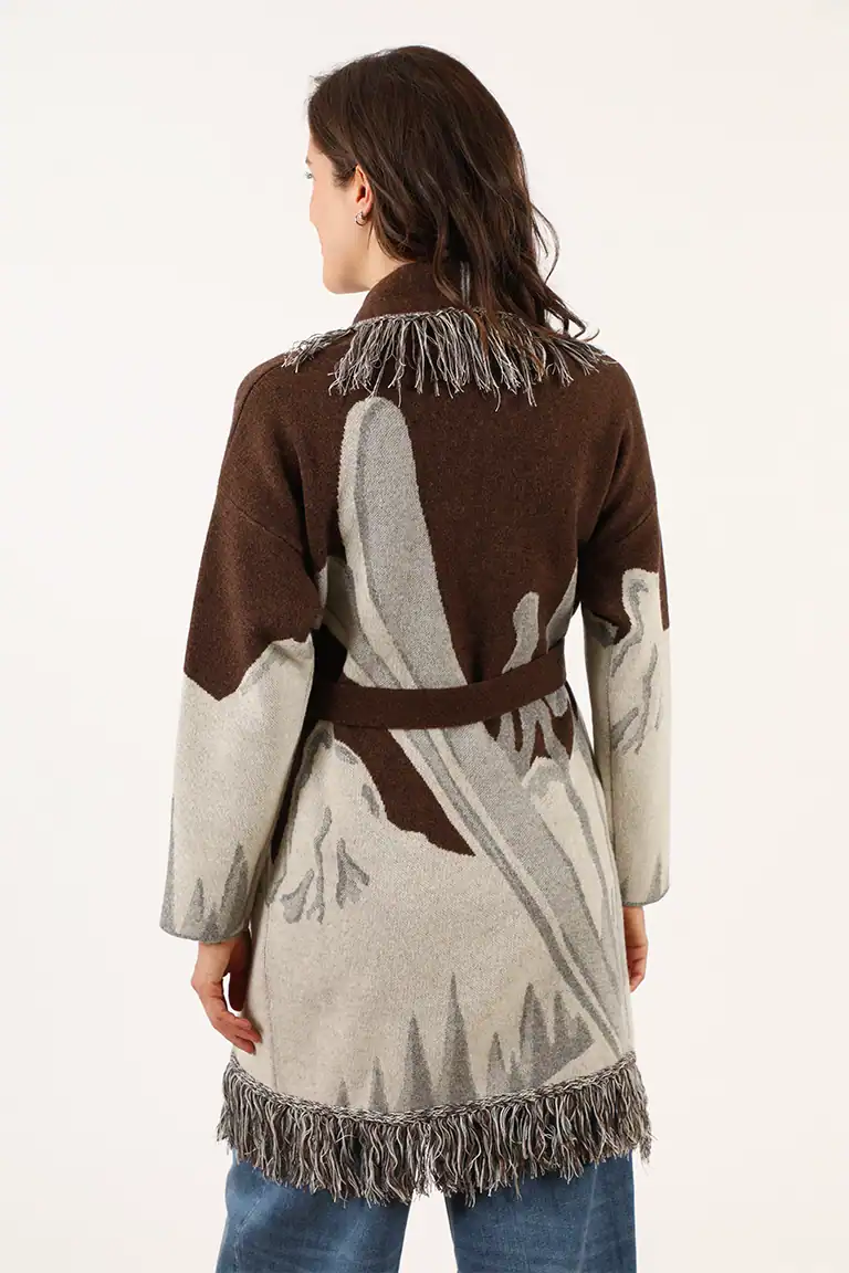 Donna indossa un cappotto in lana con motivo astratto in toni marroni e grigi, dettagli con frange sulla parte inferiore e sulle spalle, stile elegante e caldo.