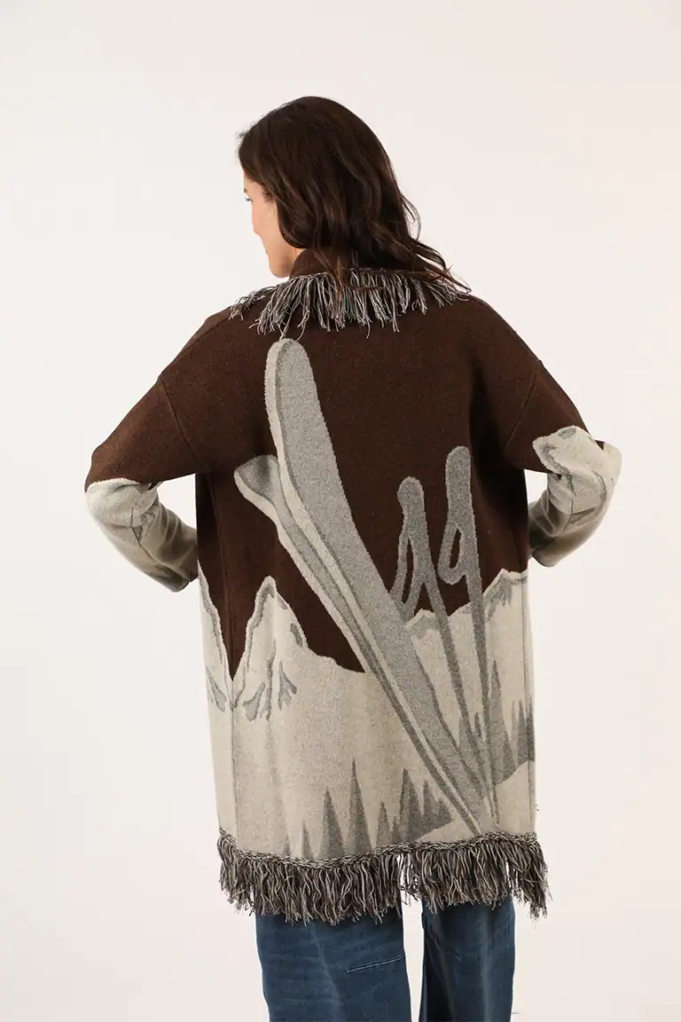 Donna indossa un maglione oversize con motivo astratto in toni marroni, grigi e beige, con frange sul bordo, perfetto per uno stile casual e elegante.