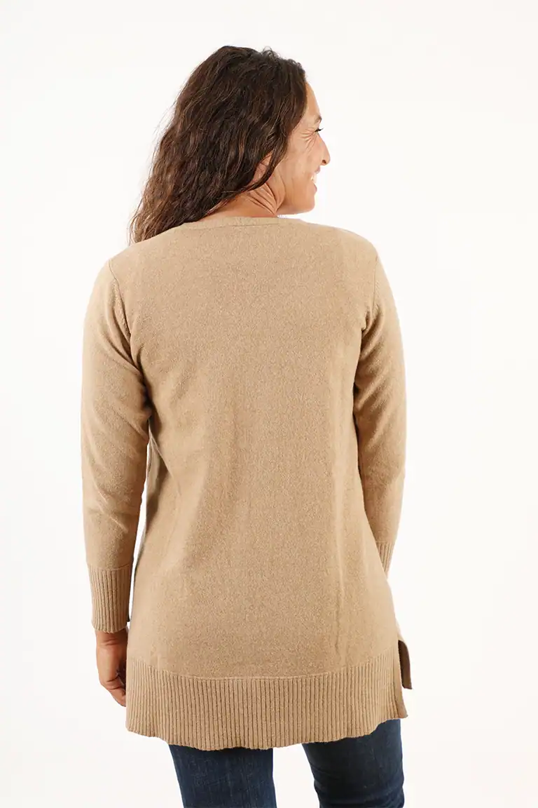 Donna indossa un maglione beige lungo in cashmere di alta qualità, perfetto per l'inverno, con dettagli eleganti e comfort superiore, ideale per look casual e sofisticati.
