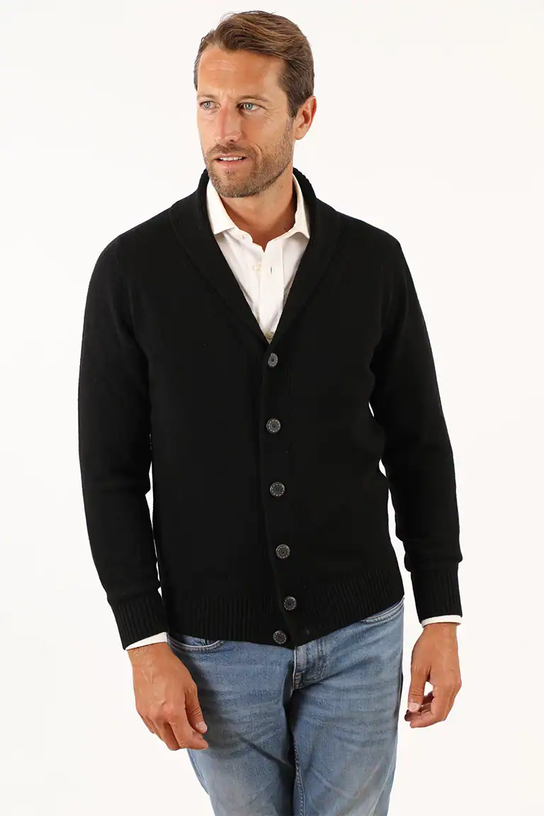 Uomo con maglione nero a bottoni, camicia bianca e jeans, stile elegante e casual, in un ambiente neutro, promuovendo la qualità dei maglioni di Maglificio Annamaria.