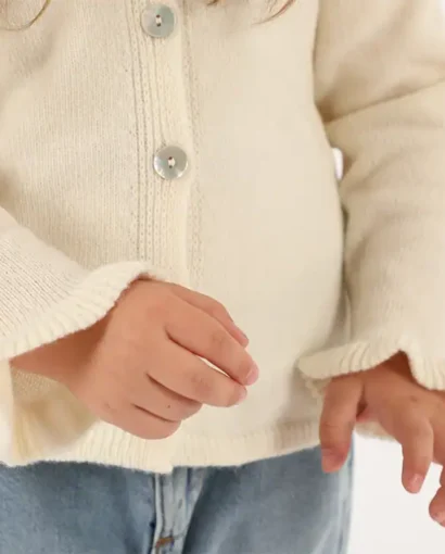 Dettaglio di un bambino che indossa un maglione beige in lana con bottoni e jeans, rappresentando abbigliamento di alta qualità del Maglificio Annamaria.