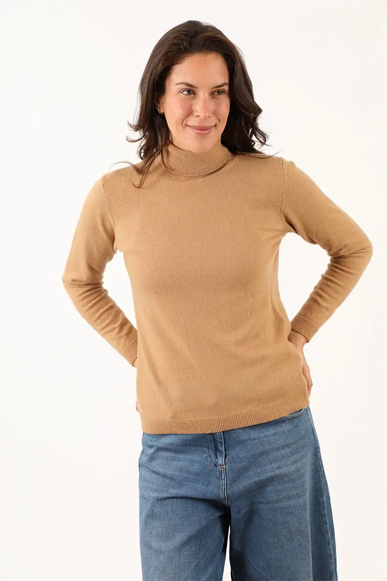 Donna indossa un maglione beige a collo alto e jeans blu, modello casual e elegante, perfetto per look autunnali e invernali, prodotto dal Maglificio Annamaria.