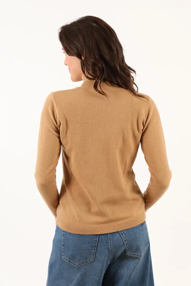 Donna indossa un maglione beige in cashmere con jeans blu, vista da dietro, in un ambiente neutro, evidenziando la qualità e il comfort dei prodotti Maglificio Annamaria.
