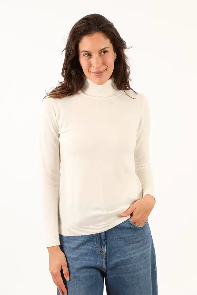 Donna indossa un maglione bianco a collo alto e jeans blu, modello casual, in uno studio con sfondo bianco, promuovendo abbigliamento di qualità di Maglificio Annamaria.