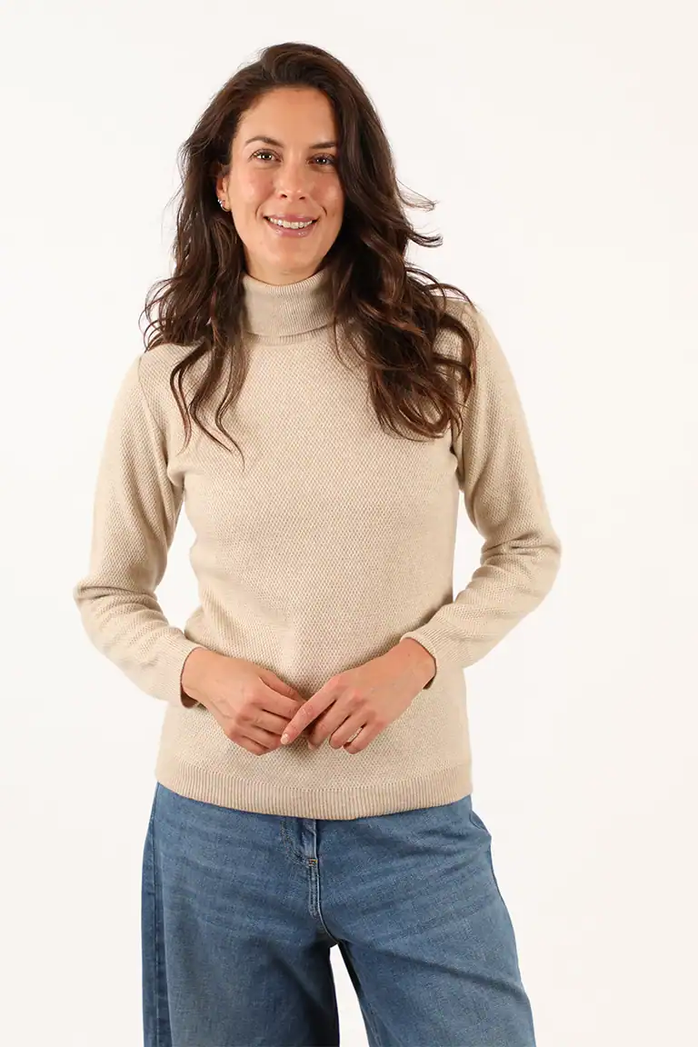 Donna sorridente indossa un maglione beige e jeans, rappresentando l'eleganza e il comfort dei capi del Maglificio Annamaria, specializzato in maglieria di alta qualità.
