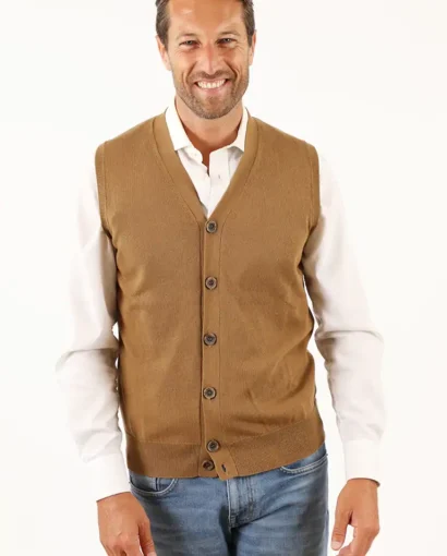 Uomo sorridente indossa un maglione senza maniche color cammello e camicia bianca, in un ambiente luminoso e professionale.