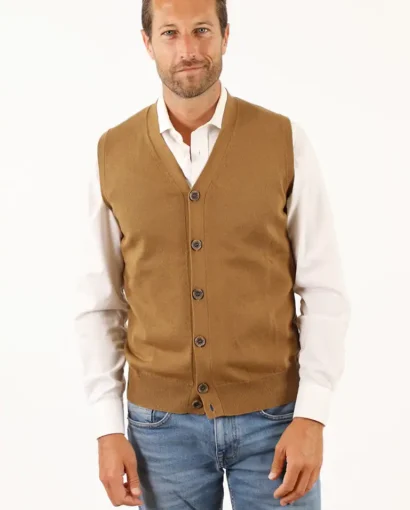 Uomo con maglione senza maniche color cammello, camicia bianca e jeans, stile elegante e casual, in primo piano, sfondo bianco.