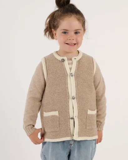 Bambina sorridente indossa un cardigan beige e crema con tasche, in un servizio fotografico di moda per Maglificio Annamaria, specializzato in maglieria di alta qualità per bambini.