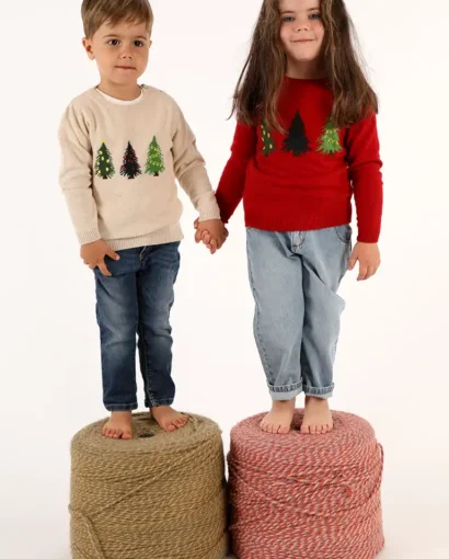 Bambini con maglioni natalizi decorati con alberi di Natale, in piedi su pouf di corda, in un servizio fotografico per Maglificio Annamaria.