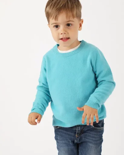 Bambino che indossa un maglione azzurro e jeans, modello casual, in studio con sfondo bianco, rappresenta abbigliamento per bambini di Maglificio Annamaria.
