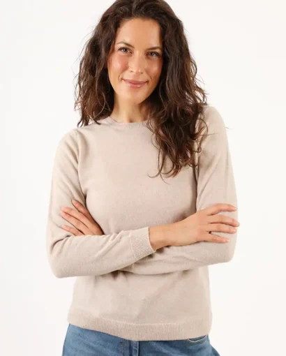 Donna sorridente indossa un maglione beige e jeans, rappresentando l'eleganza e il comfort dei prodotti Maglificio Annamaria per uno stile casual e raffinato.