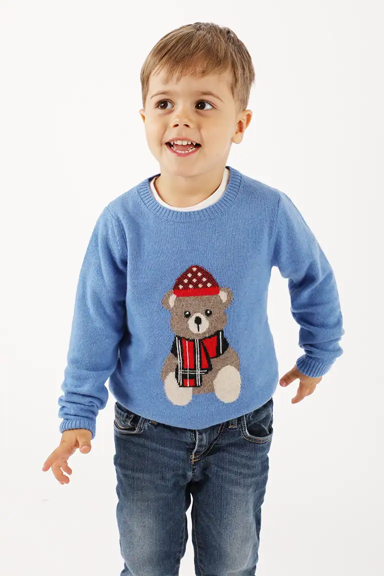 Bambino che indossa un maglione azzurro con orsetto decorativo e cappello rosso, ideale per abbigliamento bambino di qualità da Maglificio Annamaria.