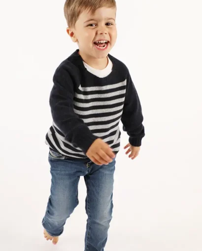 Bambino felice che corre indossando un maglione a righe nero e bianco e jeans, in uno studio con sfondo bianco, per promuovere abbigliamento per bambini di Maglificio Annamaria.