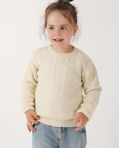 Bambina felice indossa un maglione di lana color crema e jeans chiari, modello casual e confortevole, perfetto per l'inverno, in un servizio fotografico di Maglificio Annamaria.