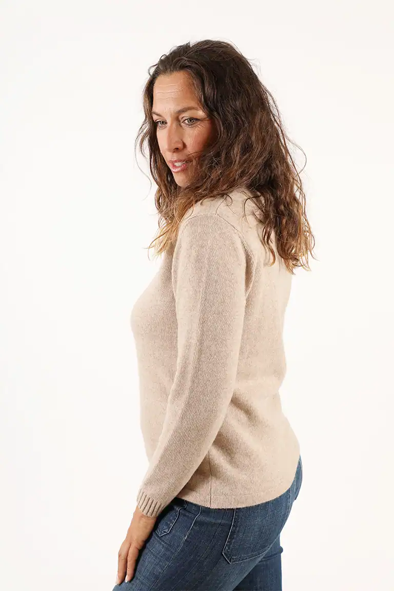 Donna indossa un maglione beige in cashmere di alta qualità, perfetto per un look elegante e confortevole, con sfondo bianco neutro.
