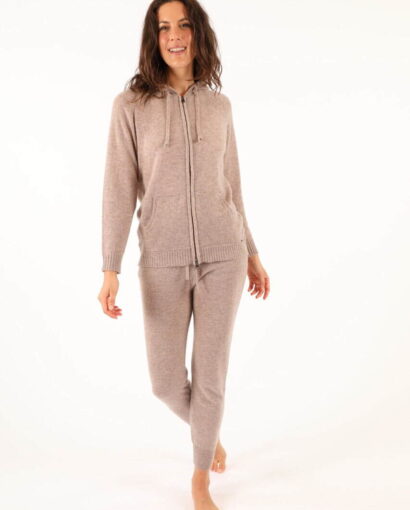 Donna indossa un completo di maglificio in tessuto caldo e morbido, ideale per l'inverno, con giacca con zip e pantaloni coordinati, in tonalità beige chiaro.