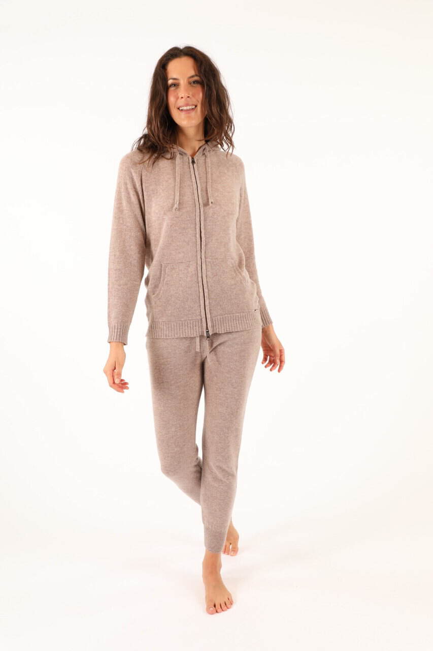 Donna indossa un completo di maglificio in tessuto caldo e morbido, ideale per l'inverno, con giacca con zip e pantaloni coordinati, in tonalità beige chiaro.