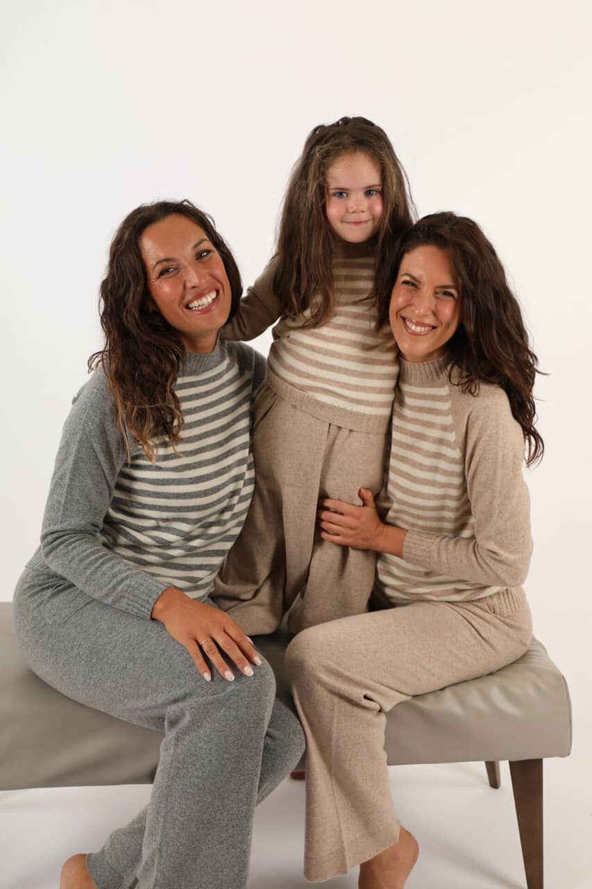Tre donne e una bambina indossano maglioni a righe in tessuto morbido, sorridendo e posando in studio per promuovere i capi di maglieria di Maglificio Annamaria.