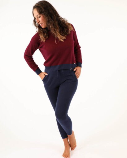 Donna indossa un maglione rosso e pantaloni blu in un ambiente neutro, promuovendo abbigliamento di alta qualità di Maglificio Annamaria per stile e comfort.