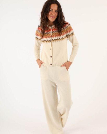 Woman wearing a cream-colored knitted cardigan with colorful geometric patterns and matching wide-leg pants, showcasing stylish knitwear from Maglificio Annamaria.