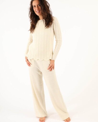 Donna sorridente indossa un maglione e pantaloni in lana color crema, moda elegante e confortevole di Maglificio Annamaria per look invernali sofisticati.